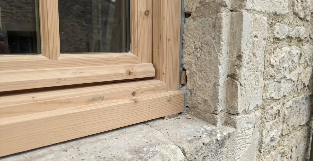 Gros plan macro sur une rainure de feuillure creusée dans un mur en pierre traditionnelle, montrant le détail du logement du dormant de fenêtre